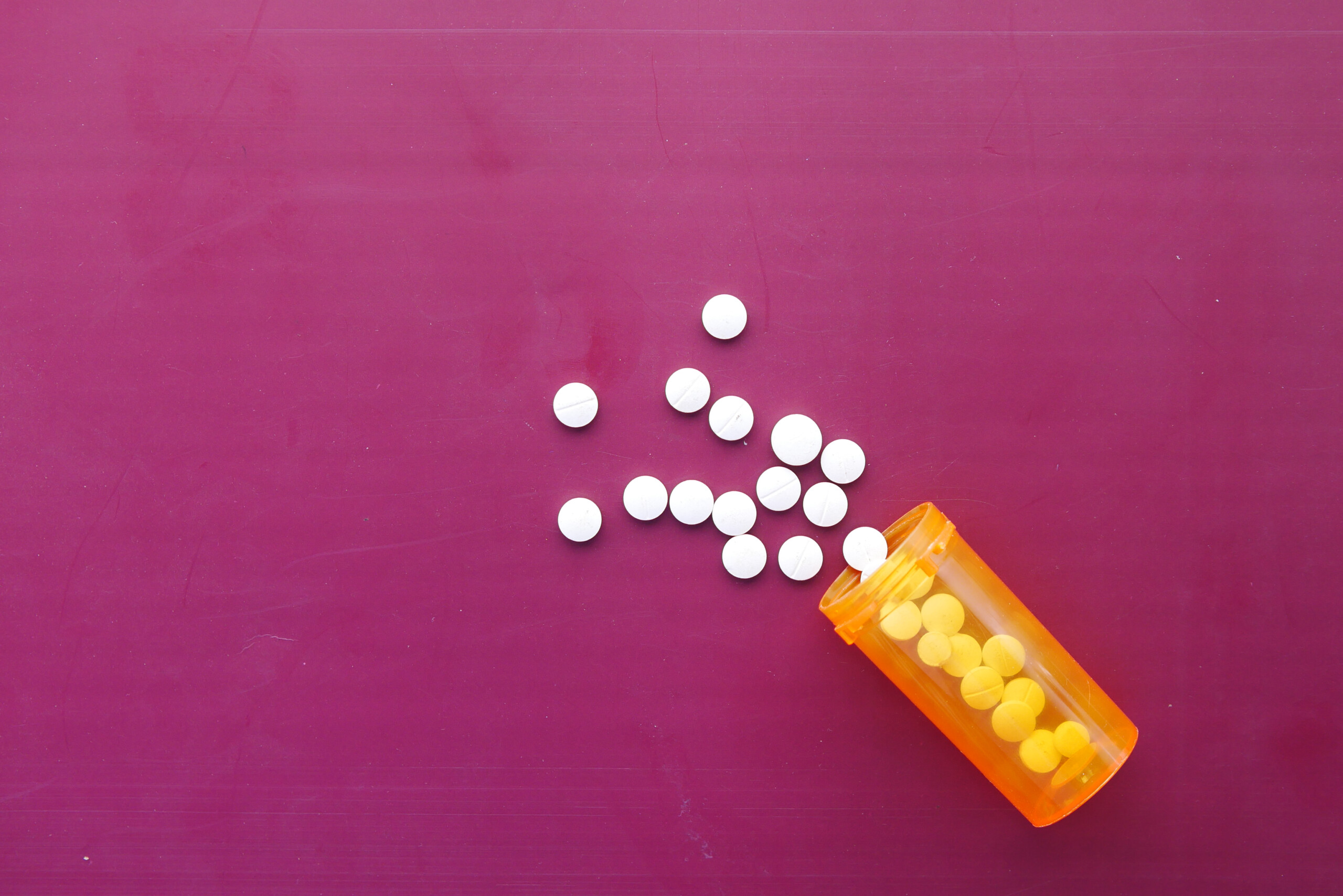 Weiße Tabletten ausgeschüttet auf pinken Hintergrund